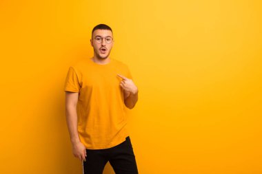 Genç ve yakışıklı bir adam ağzı açık, şaşkın ve şaşırmış görünüyor, düz arkaplan karşısında kendini işaret.