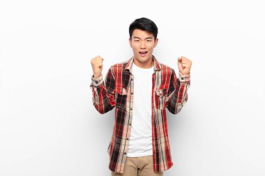 Genç Çinli adam mutlu, pozitif ve başarılı hissediyor, zaferi kutluyor, başarılar ya da düz renkli duvara karşı iyi şanslar.