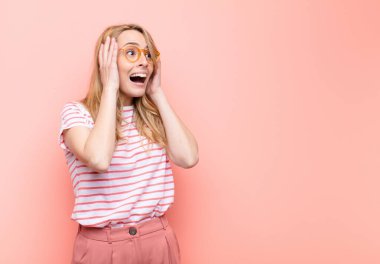 Genç, güzel sarışın kadın mutlu, heyecanlı ve şaşırmış hissediyor. İki eli de düz duvara bakıyor.