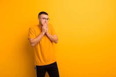 Genç yakışıklı adam mutlu ve heyecanlı, şaşırmış ve hayrete düşmüş elleriyle ağzını kapatmış, düz arkaplan karşısında sevimli bir ifadeyle kıkırıyor.