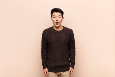 Genç Çinli adam şok olmuş ya da şaşırmış görünüyor, ağzı açık bir şekilde düz duvara karşı 