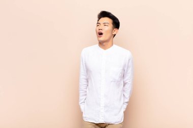 Genç Çinli adam öfkeyle bağırıyor, agresif bir şekilde bağırıyor, stresli ve sinirli görünüyor.