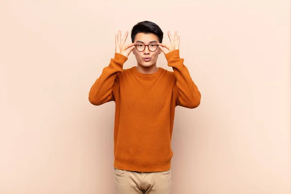 若い中国人男性はショックを受け驚き驚きましたフラットカラーの壁に対して信じられないほどの表情でメガネを持っています — ストック写真