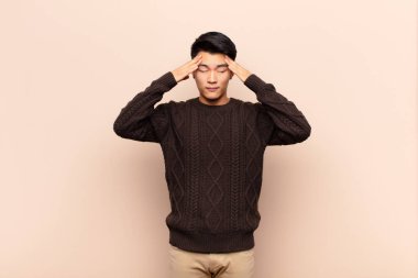 Genç Çinli adam konsantre, düşünceli ve ilham verici görünüyor, beyin fırtınası yapıyor ve düz renk duvarına karşı elleri alnında hayal ediyor.