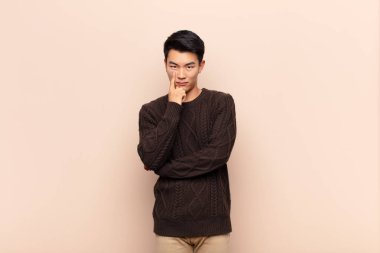 Genç Çinli adam sana göz kulak oluyor, güvenmiyor, izliyor ve düz renkli duvarlara karşı tetikte oluyor.