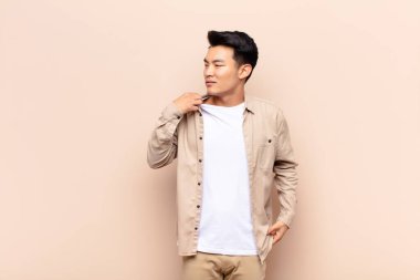 Genç Çinli bir adam stresli, endişeli, yorgun ve hayal kırıklığına uğramış, gömlek boyunlu, düz renkli duvara karşı sorunlu görünüyor.