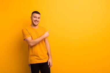 Genç ve yakışıklı adam heyecanlı ve şaşırmış görünüyor. Yana ve yukarıya doğru düz arkaplana uzayı kopyalıyor.