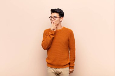 Genç Çinli bir adam sessizlik ve sessizlik istiyor, parmaklarıyla ağzının önünde işaret ediyor, 