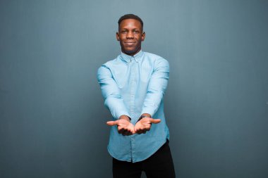 Genç Afro-Amerikan siyahi adam mutlu bir şekilde gülümsüyor, arkadaş canlısı, kendine güvenen, olumlu bakışlı, bir nesne ya da konsept sunuyor ve gösteriyor.