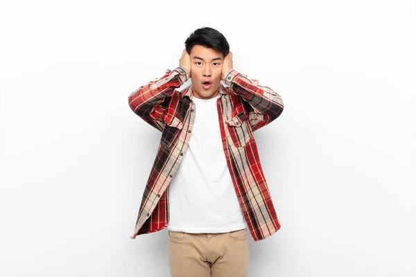 若い中国人の男は不快なショック 恐怖や心配 口を大きく開いて 平らな色の壁に対して手で両耳をカバー — ストック写真