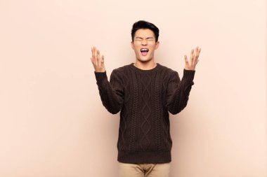 Genç Çinli adam öfkeyle bağırıyor, stres altında ve elleri havada neden düz duvara yaslandığımı söylüyor.