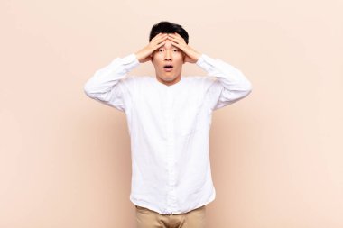 Genç Çinli adam dehşete kapılmış ve şok olmuş hissediyor. Düz renkli duvara karşı yapılan bir hatadan dolayı el ele tutuşup panikliyor.