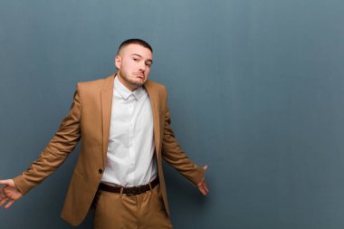 Genç, yakışıklı iş adamı bilgisiz ve şaşkın hissediyor, hiçbir fikri yok, düz arkaplan karşısında aptal ya da aptal bir bakışla tamamen kafası karışmış.