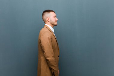 Profil görünümlü genç bir adam uzayı kopyalamaya çalışıyor, düşünüyor, hayal ediyor ya da düz duvara karşı hayal kuruyor.