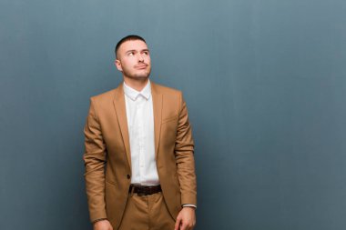 Genç ve yakışıklı iş adamı kafası karışmış görünüyor, merak ediyor ya da bir sorunu çözmeye çalışıyor ya da düz arkaplan üzerinde düşünüyor.