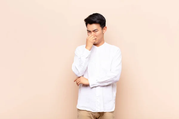 若い中国人の男は フラットカラーの壁に対して悪臭や不快な臭いを避けるために鼻を保持 うんざりしている — ストック写真