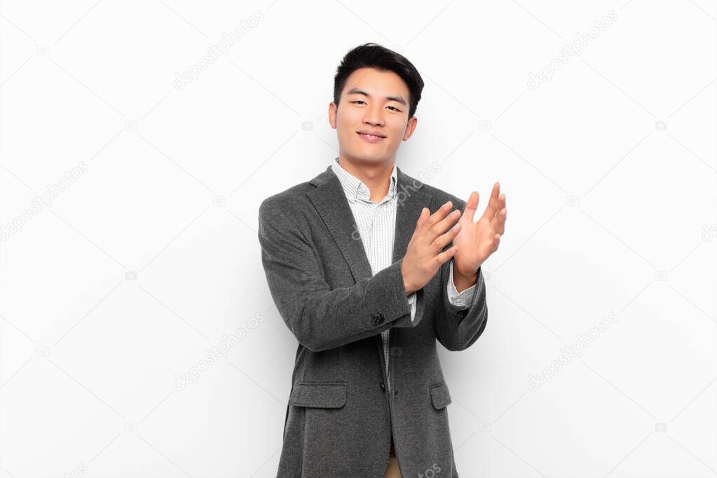 young chinese man feeling happy and successful, smiling and clapping hands, saying congratulations with an applause against flat color wall