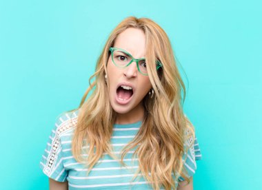 young pretty blonde woman looking shocked, angry, annoyed or disappointed, open mouthed and furious against flat color wall clipart