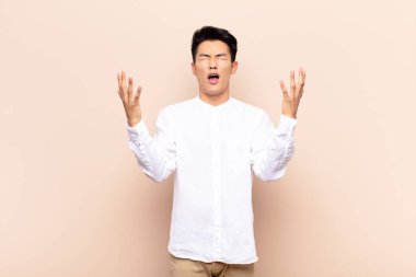 Genç Çinli adam öfkeyle bağırıyor, stres altında ve elleri havada neden düz duvara yaslandığımı söylüyor.