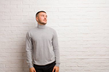 Endişeli, kafası karışık, budala bir ifadeyle genç yakışıklı bir adam kopya alanı arıyor, düz arkaplana karşı şüpheyle bakıyor.