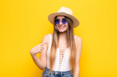 Genç ve güzel bir kadın gururlu, kendinden emin ve mutlu görünüyor, gülümsüyor ve kendini işaret ediyor ya da bir numaralı işareti yapıyor.