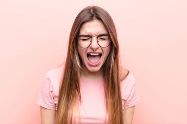 Genç ve güzel bir kadın agresif bir şekilde bağırıyor. Kızgın, sinirli, öfkeli ya da sinirli görünüyor. Pembe duvara karşı hayır diye bağırıyor.