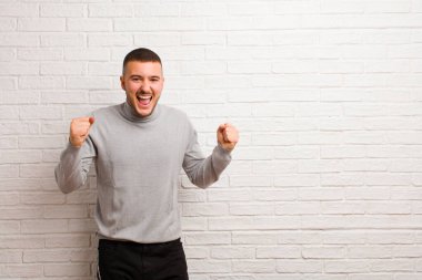 Genç yakışıklı adam mutlu, şaşırmış ve gururlu, bağırıyor ve başarıyı kutluyor.