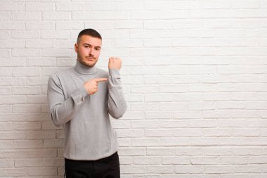 Genç, yakışıklı, sabırsız ve sinirli bir adam, saati gösteriyor, dakiklik istiyor, düz arkaplan karşısında tam zamanında olmak istiyor.