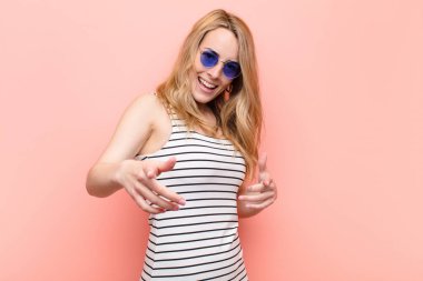 Genç, güzel, sarışın bir kadın kendini mutlu, sakin, rahat ve başarılı hissediyor, kameraya bakıyor, düz renkli duvara karşı seni seçiyor.