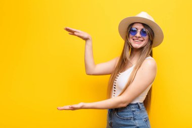 Genç ve güzel bir kadın bir objeyi iki eliyle fotokopi alanında tutuyor, bir objeyi gösteriyor, sunuyor ya da reklamını yapıyor.