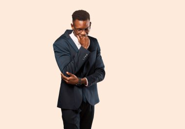 Afro-Amerikan iş adamı ciddi, düşünceli ve endişeli hissediyor, elleri bej duvara yaslanmış bir şekilde yan bakıyor.