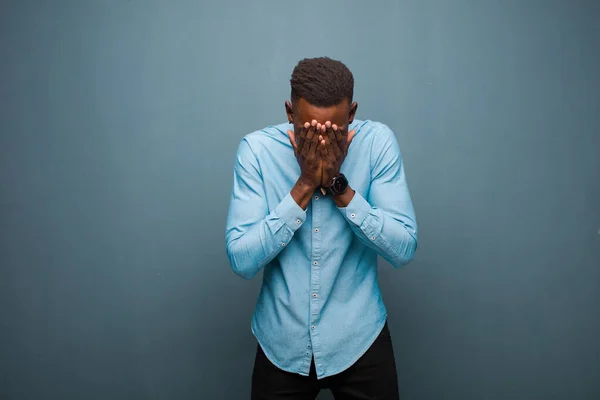 young african american black man feeling sad, frustrated, nervous and depressed, covering face with both hands, crying