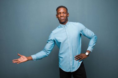 Genç Afro-Amerikan siyahi adam mutlu ve neşeli hissediyor, gülümsüyor ve hoş geldiniz diyor, sizi içeri davet ediyor grunge duvarına karşı dostça bir hareketle