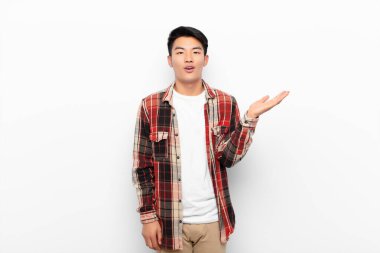 Genç Çinli adam mutlu, şaşırmış ve neşeli hissediyor, pozitif bir tavırla gülümsüyor, düz renkli duvara karşı bir çözüm ya da fikir buluyor.