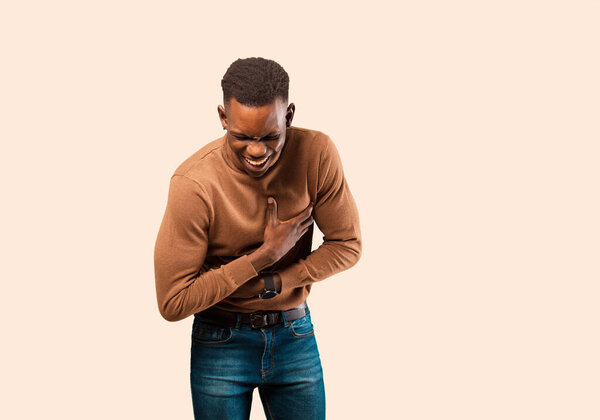 Young african american black man laughing out loud at some hilarious joke, feeling happy and cheerful, having fun against beige wall