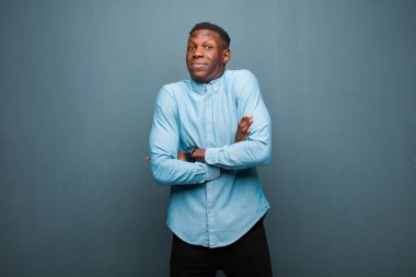 Genç Afrikalı Amerikalı siyah adam omuz silkiyor, kafası karışık ve kararsız, kolları bağlı ve şaşkın görünüyor.