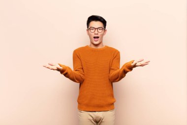 Genç Çinli adam şok olmuş, şaşırmış, endişeli ve paniklemiş hissediyor. Düz renkli duvara karşı stresli ve dehşetli bir bakışla bakıyor.