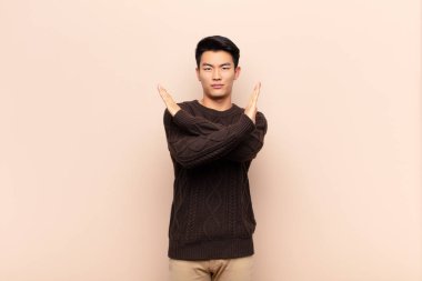 Genç Çinli adam senin bu tavrından rahatsız ve bıkkın görünüyor. Yeter! Eller önde çapraz, düz renkli duvara karşı durmanı söylüyor.