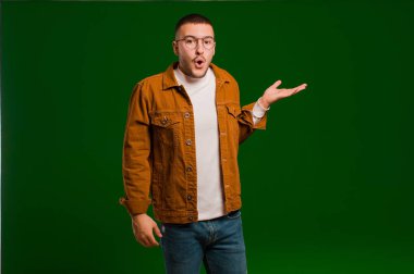 Genç yakışıklı adam şaşırmış ve şok olmuş görünüyor, çenesi düşmüş ve düz arkaplana karşı eli açık bir objeyi tutuyor.