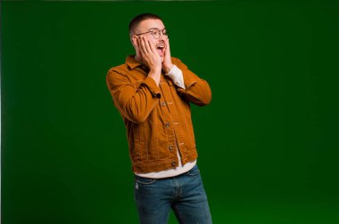 Genç yakışıklı adam mutlu, heyecanlı ve şaşırmış hissediyor, iki eli de düz arkaplanda yana bakıyor.