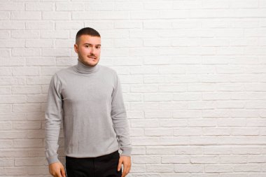 Şaşkın ve kafası karışmış genç bir adam gergin bir hareketle dudağını ısırıyor, düz duvara karşı sorunun cevabını bilmiyor.