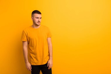 Genç, yakışıklı bir adam üzgün, üzgün ya da kızgın ve olumsuz bir tavırla yan yana bakıyor, düz arkaplan karşısında anlaşmazlık içinde.