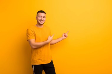 Genç yakışıklı adam mutlu bir şekilde gülümsüyor ve her iki elinde fotokopi odasında düz arkaplan karşısında nesne gösteriyor.