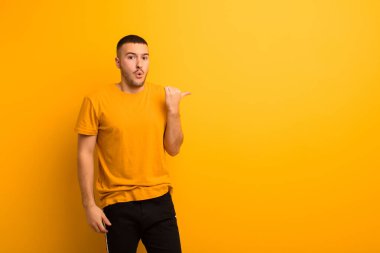 Genç ve yakışıklı adam inançsızlıktan şaşkın şaşkın bakıyor, yan taraftaki objeyi işaret ediyor ve diyor ki vay be, düz arkaplan karşısında inanılmaz.