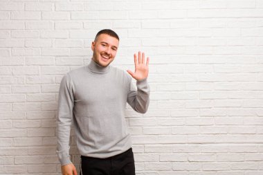 Genç yakışıklı adam mutlu ve neşeli bir şekilde gülümsüyor, el sallıyor, seni selamlıyor, ya da düz arkaplanda veda ediyor.