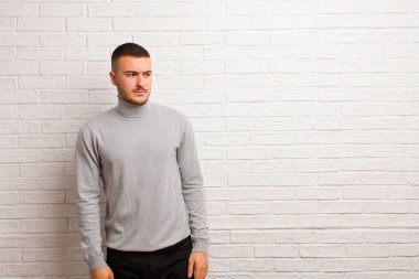 Genç, yakışıklı bir adam üzgün, üzgün ya da kızgın ve olumsuz bir tavırla yan yana bakıyor, düz arkaplan karşısında anlaşmazlık içinde.