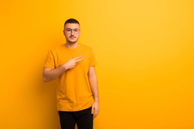 Genç yakışıklı adam mutlu, pozitif ve başarılı hissediyor, göğsünde V şeklinde eller yapıyor, düz arkaplana karşı zafer ya da barış gösteriyor.