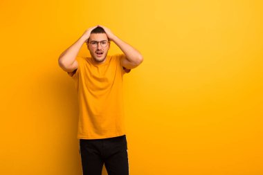 Dehşete kapılmış ve şok olmuş hisseden genç yakışıklı bir adam, el ele tutuşuyor ve düz arkaplanda yapılan bir hatada panikliyor.