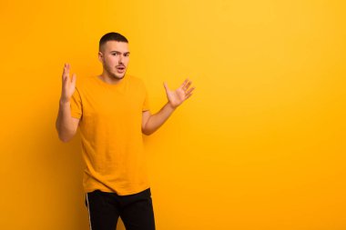 Genç yakışıklı adam şaşırmış ve şaşırmış görünüyor, düz arkaplan karşısında inanılmaz bir şey fark ettiğinde çene şaşkın