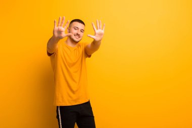 Genç yakışıklı adam gülümsüyor ve arkadaş canlısı görünüyor, onuncu ya da onuncu numarayı gösteriyor, düz arkaplanda geriye doğru sayıyor.